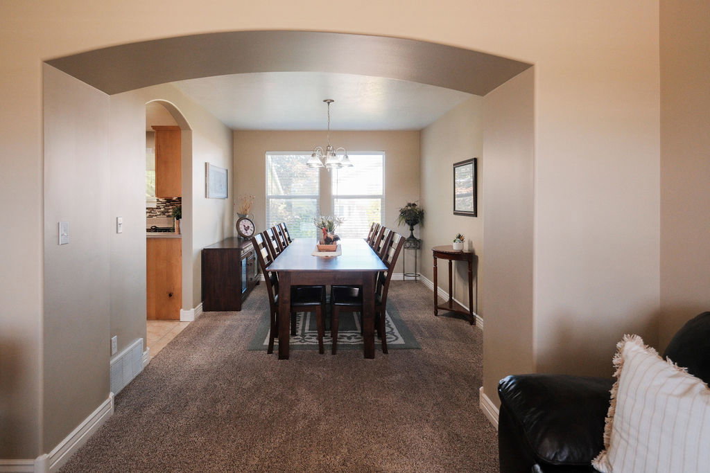 Expansive dining area featuring plush carpeting, an arched entryway, and a large window with blinds