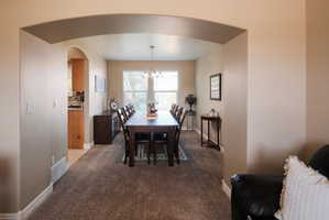 Expansive dining area featuring plush carpeting, an arched entryway, and a large window with blinds