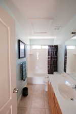Bathroom featuring a single vanity with wood-finish cabinetry and a white countertop, a white porcelain sink, tile flooring, and a white bathtub with an integrated shower