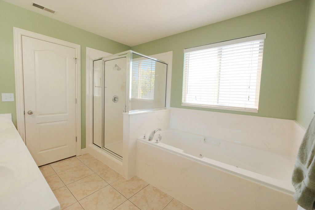 Full bathroom featuring a built-in soaking tub, a glass-enclosed shower, a large window with blinds, and tile flooring