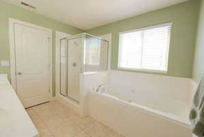 Full bathroom featuring a built-in soaking tub, a glass-enclosed shower, a large window with blinds, and tile flooring