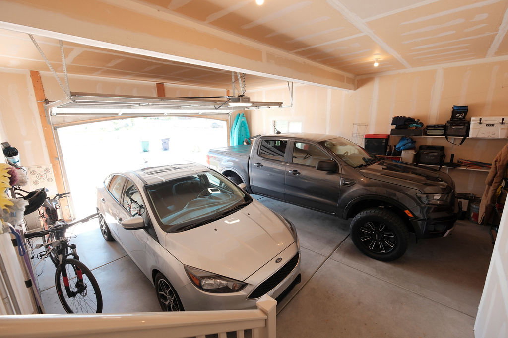 Spacious two-car garage with overhead lighting, unfinished drywall, and an open garage door