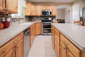 Kitchen featuring light wood cabinetry with silver-tone hardware, a white composite sink, and a multi-tone tile backsplash