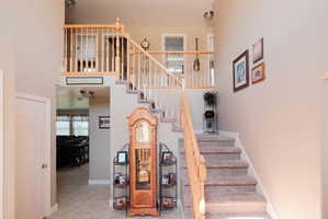 Two-story foyer featuring a carpeted staircase with light wood banister and balusters, tile flooring, and a recessed ceiling light