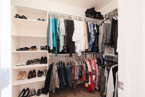 Walk-in closet featuring white shelving, multiple hanging rods, and neutral carpet flooring