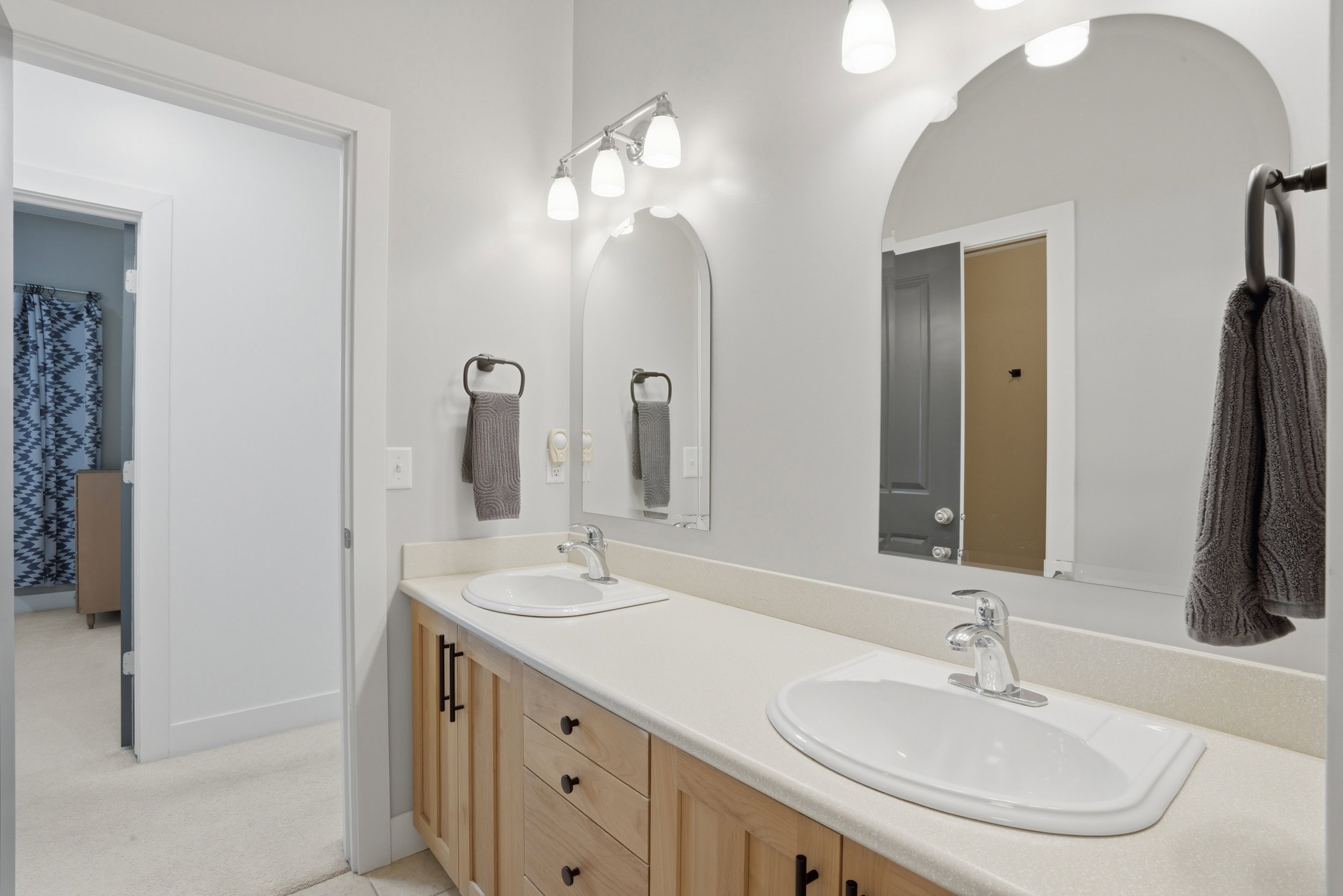 Double vanity with integrated white sinks, light wood cabinetry, and chrome fixtures