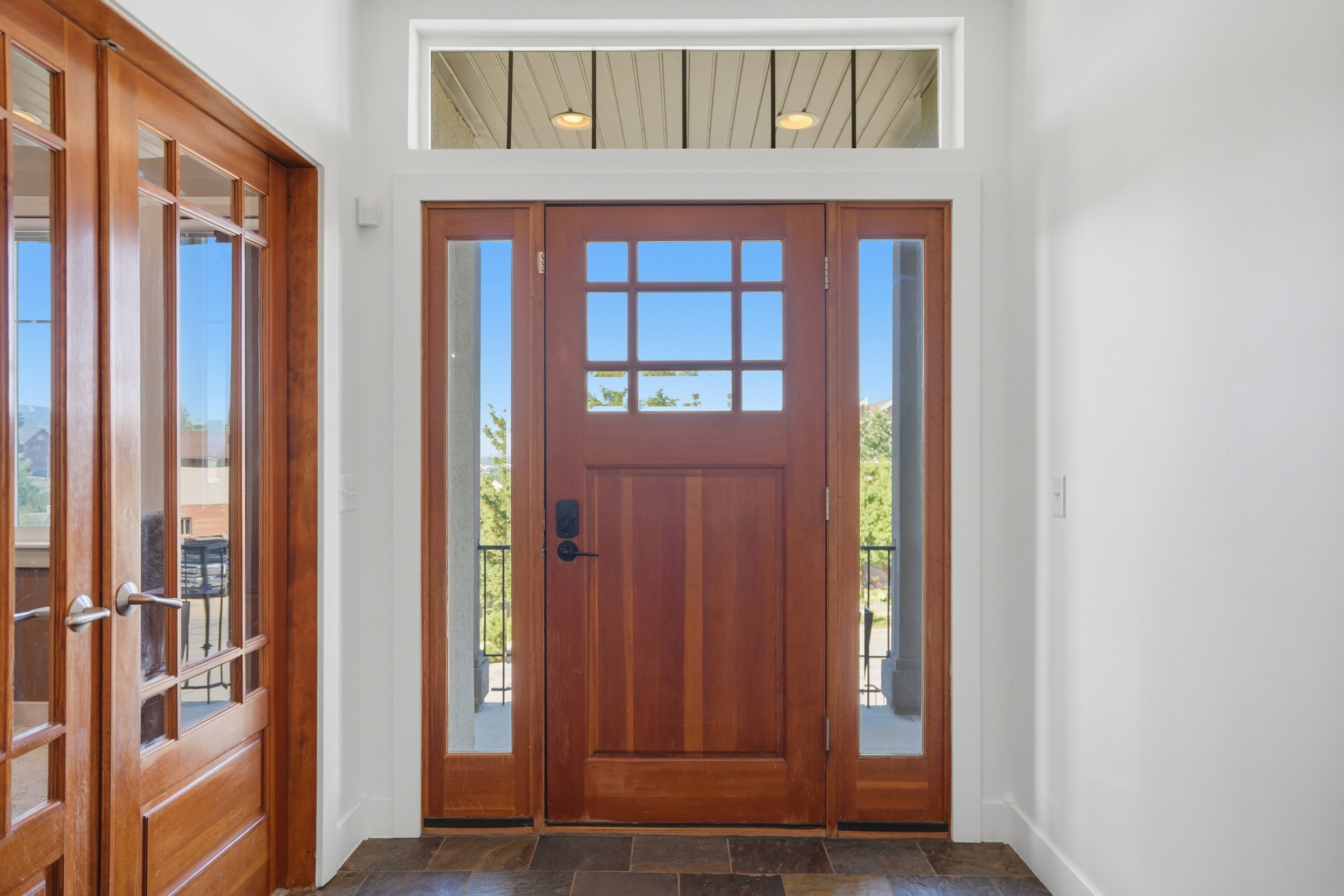 Warm wood entry door with sidelights and transom window, complemented by slate tile flooring is a warm welcome into your home