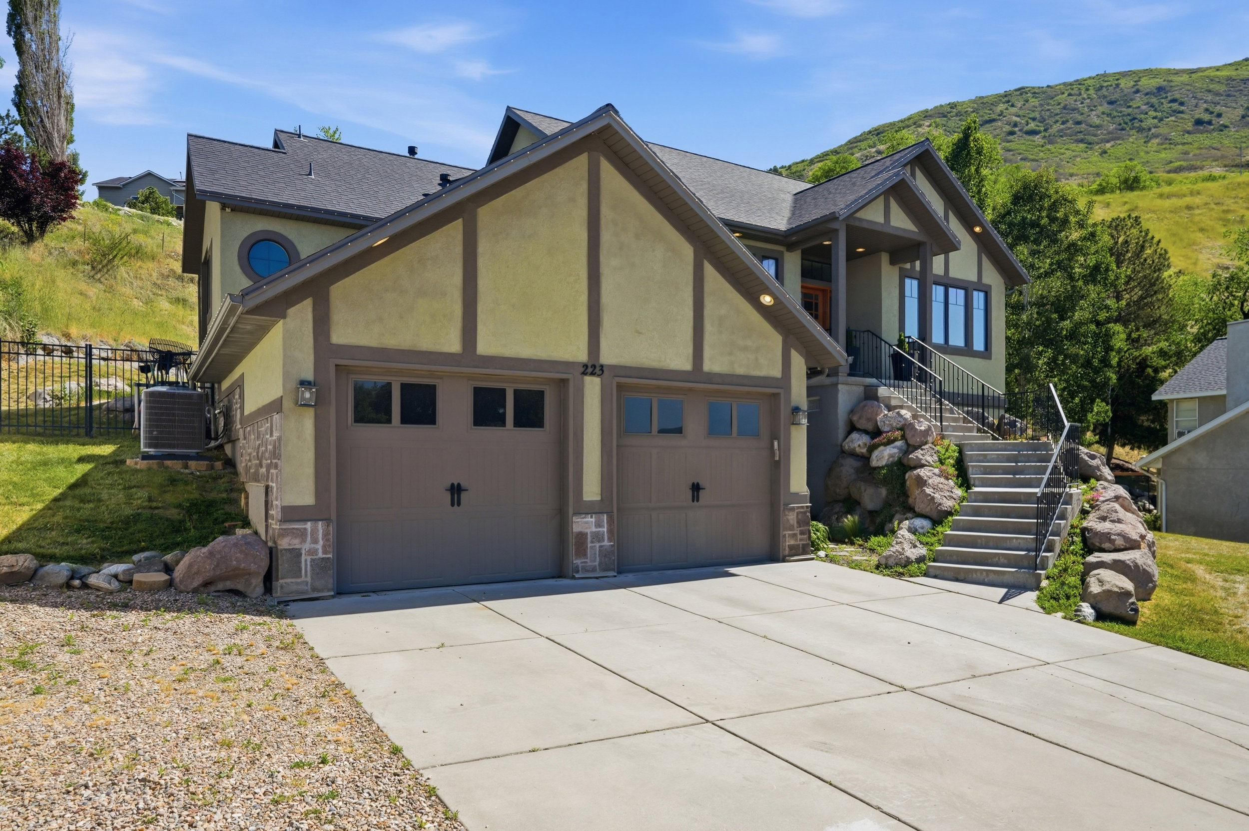 Stucco, south facing home featuring a two-car garage, concrete driveway, and a front entry with stone steps and metal railings. The view from the porch is a must see!