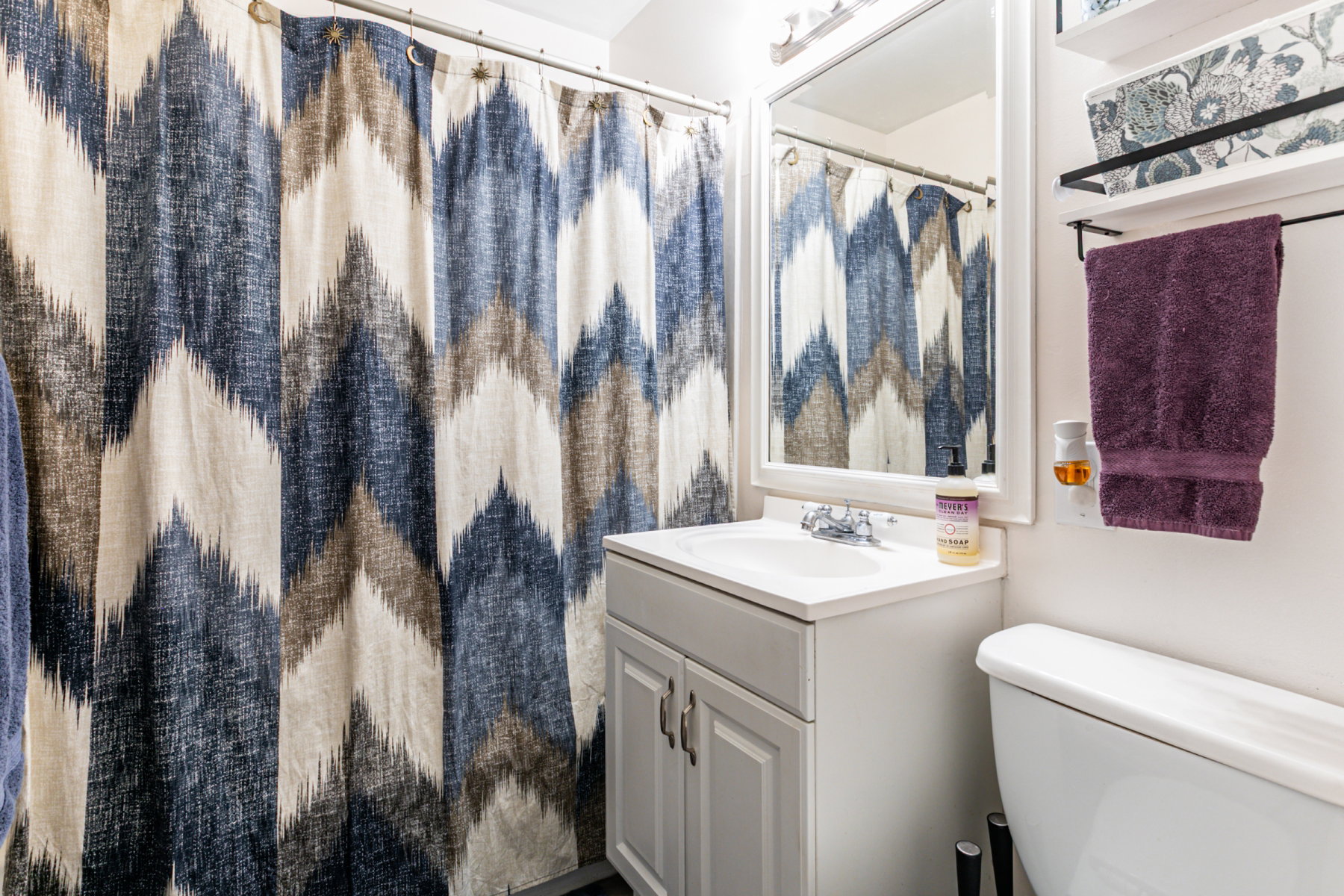 Bathroom featuring a white vanity with integrated sink, a framed mirror, shelves and overhead vanity lighting