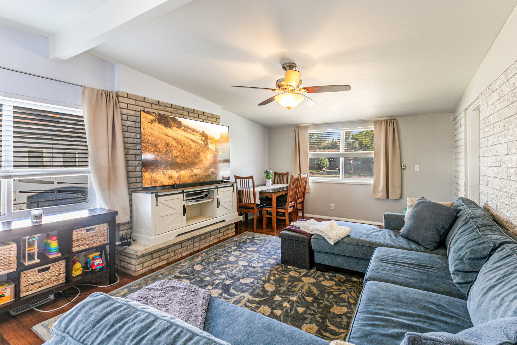 Family area featuring wood like flooring, exposed ceiling beams, and a exposed brick  wall with a large wood burning fireplace.