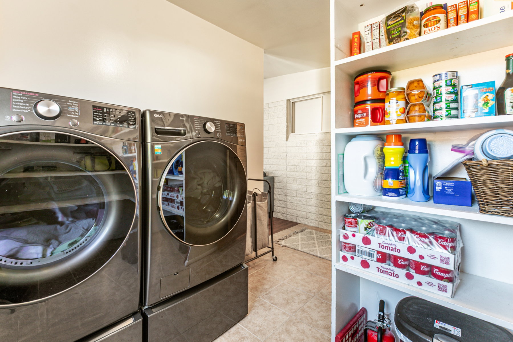 Laundry area featuring tile flooring, built-in shelving, and a white brick-patterned wall