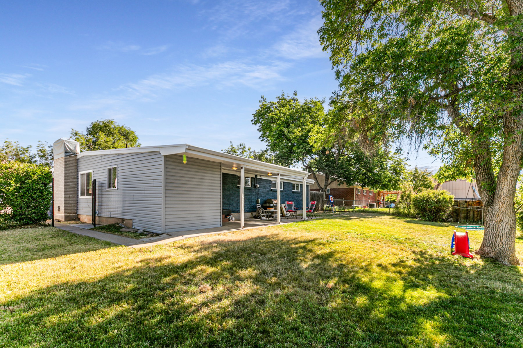 Expansive backyard featuring a large green lawn, mature shade trees, and a covered patio area with a light-colored roof