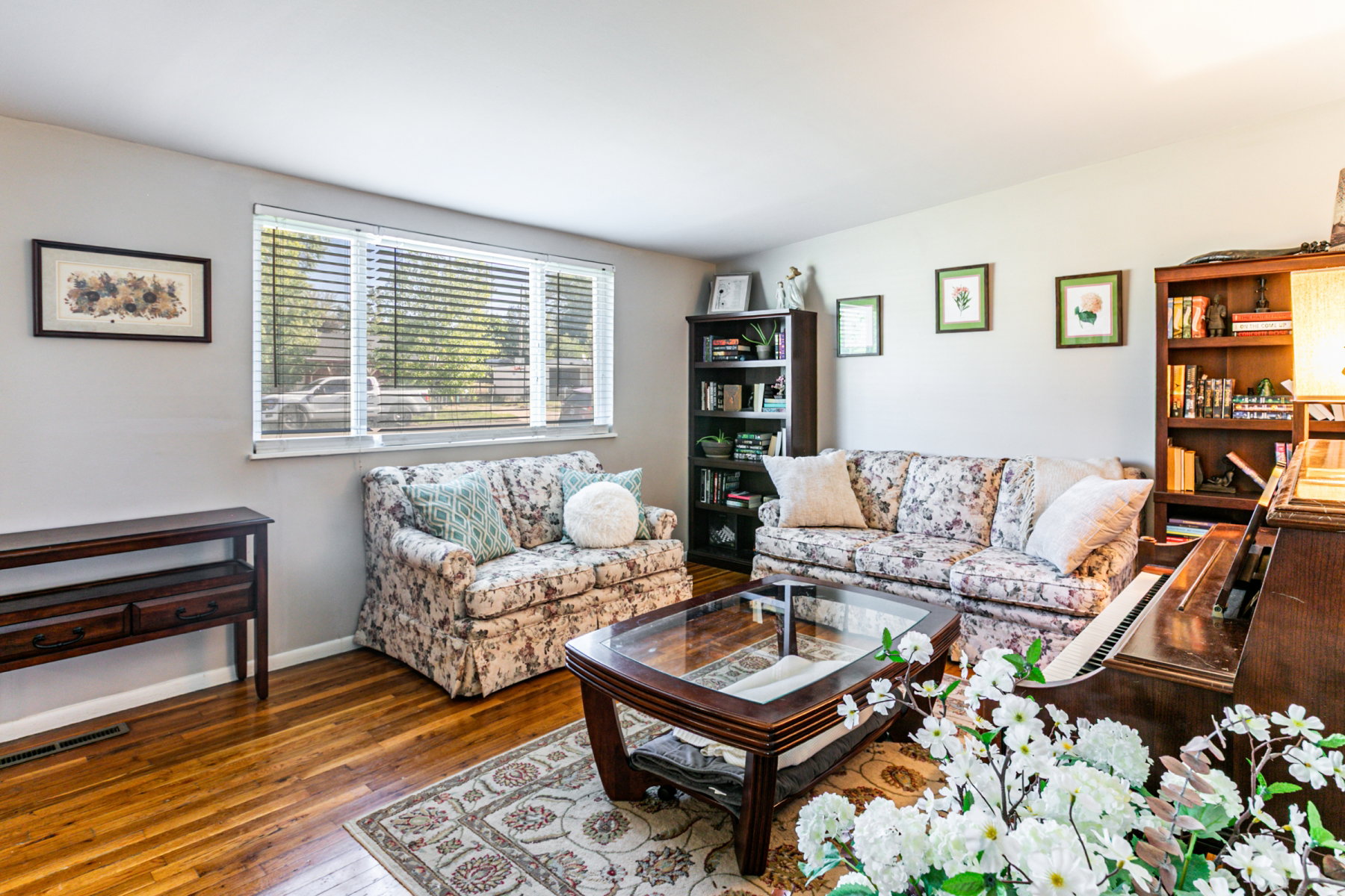 Spacious living area featuring wood flooring, a large window with blinds, and light-toned walls