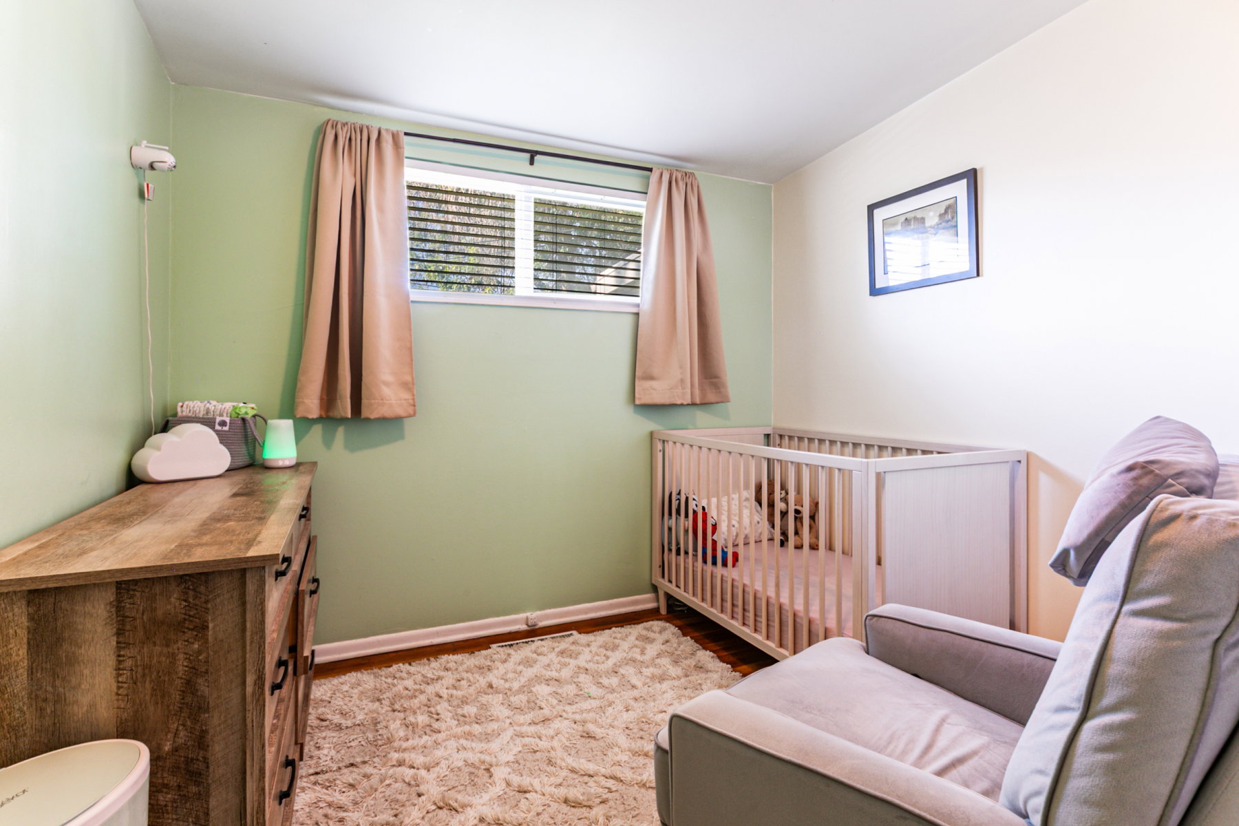 Bedroom with light green and white painted walls, hardwood flooring, and a window with horizontal blinds.