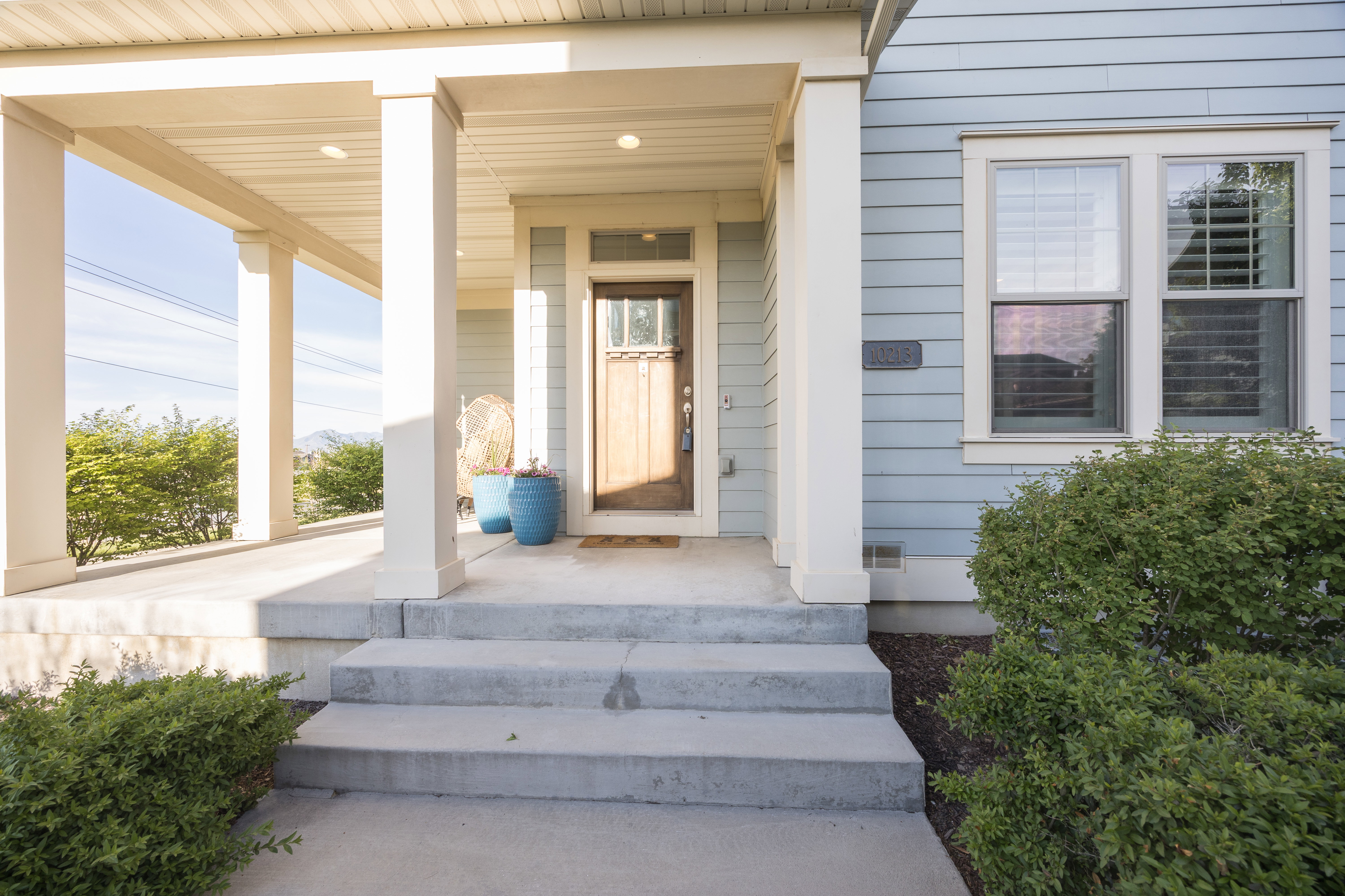 Covered front porch with substantial columns, a natural wood-finish door with glass inserts, light blue horizontal siding, and concrete steps