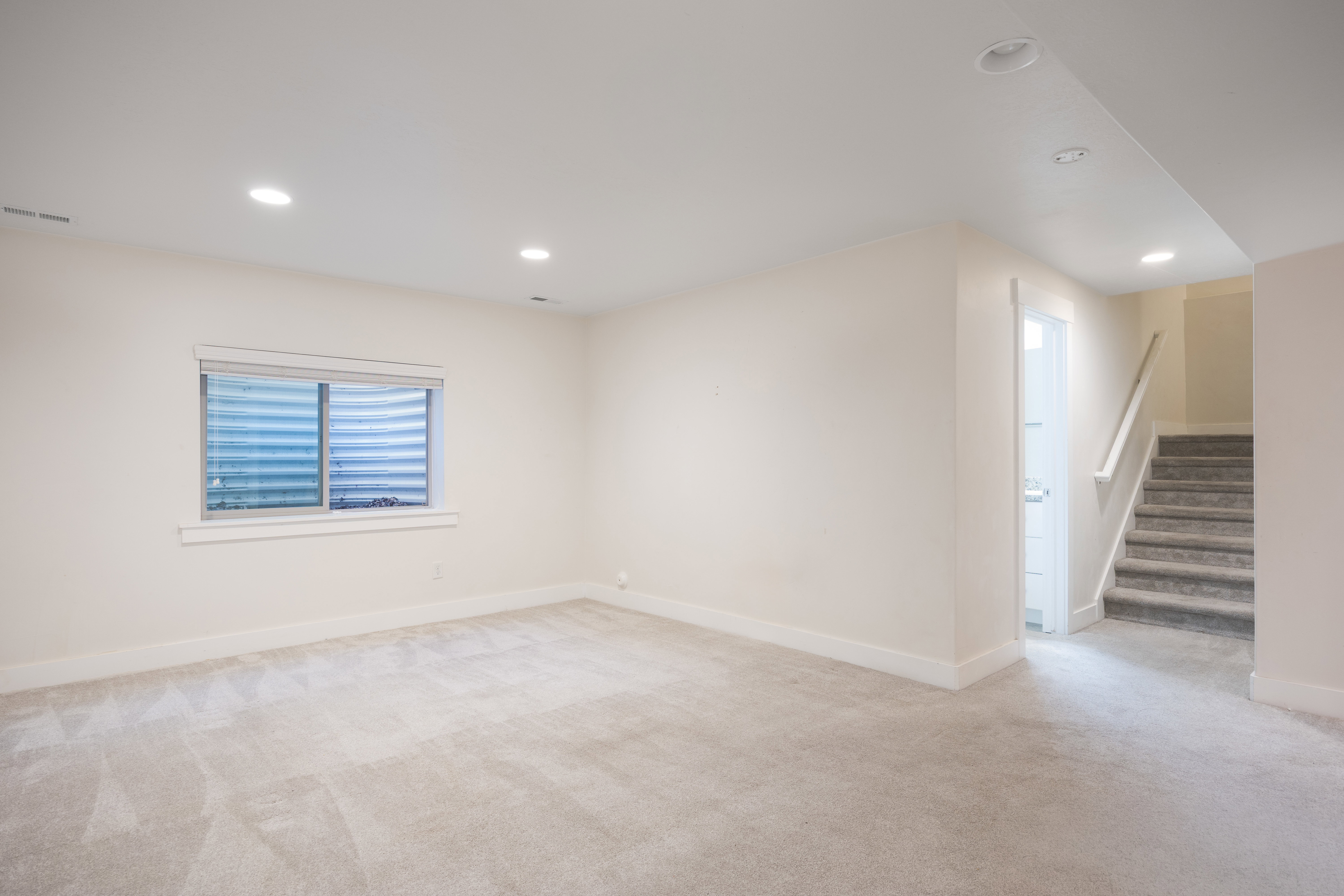 Spacious room featuring light-toned carpeting, recessed lighting, and a basement window
