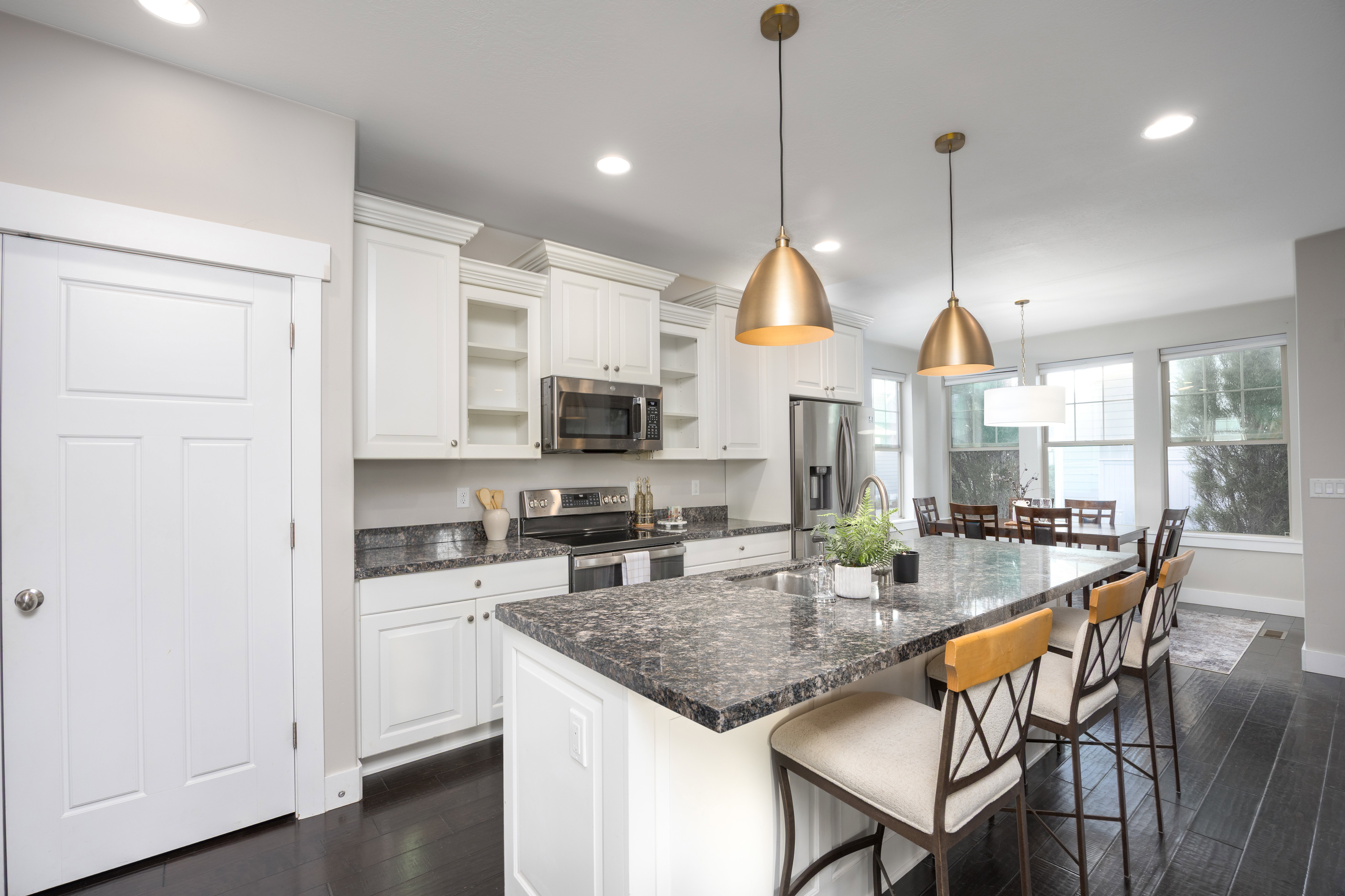 Kitchen featuring an expansive island with a dark-toned countertop, white cabinetry, stainless steel appliances, dark wood-finish flooring, and recessed lighting
