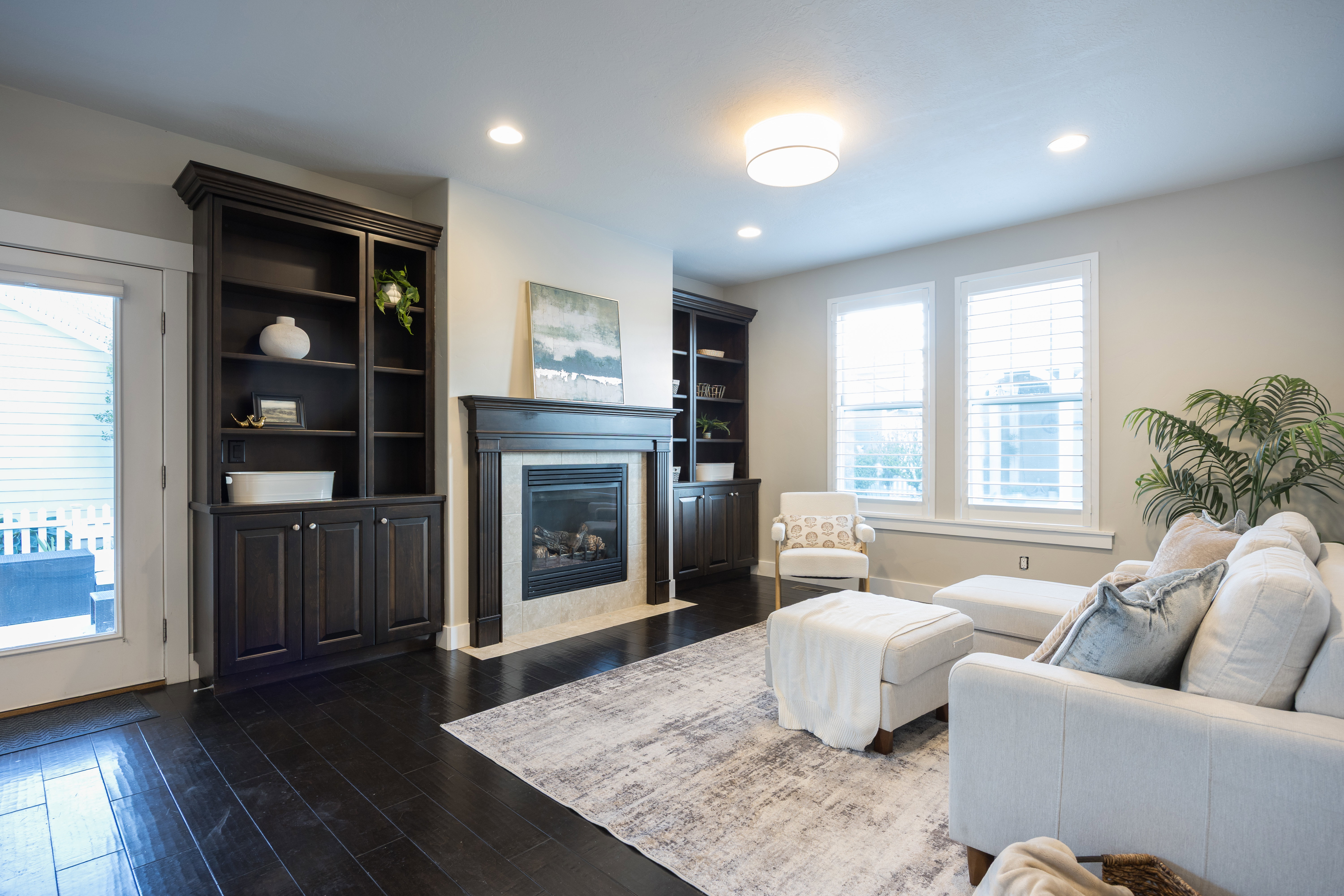 Living space featuring dark wood-finish flooring, a built-in fireplace with a light-toned surround, recessed lighting, and white plantation shutters on multiple windows