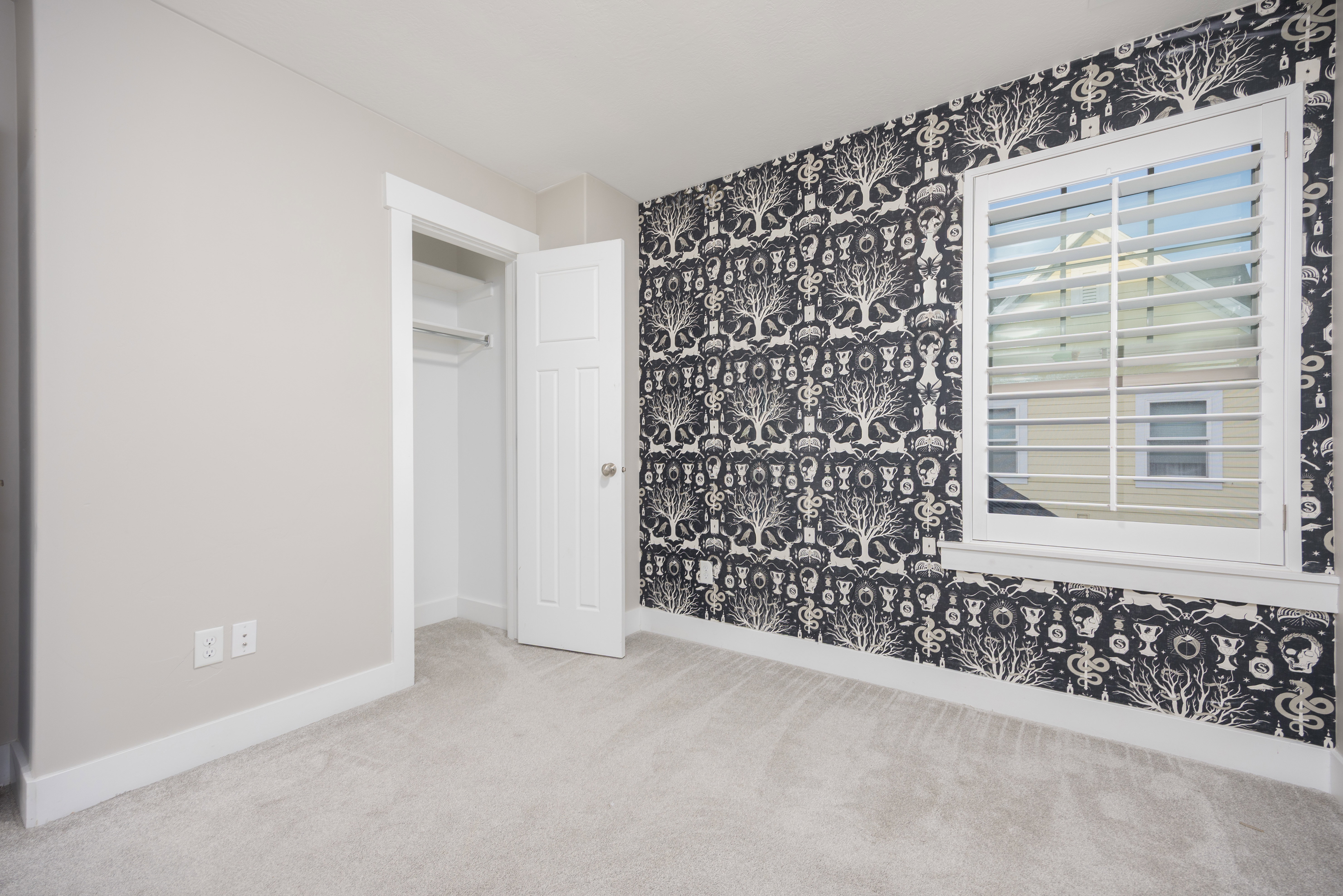 Bedroom featuring a patterned accent wall, light-toned carpeting, a window with plantation shutters, a white paneled door, and an open closet