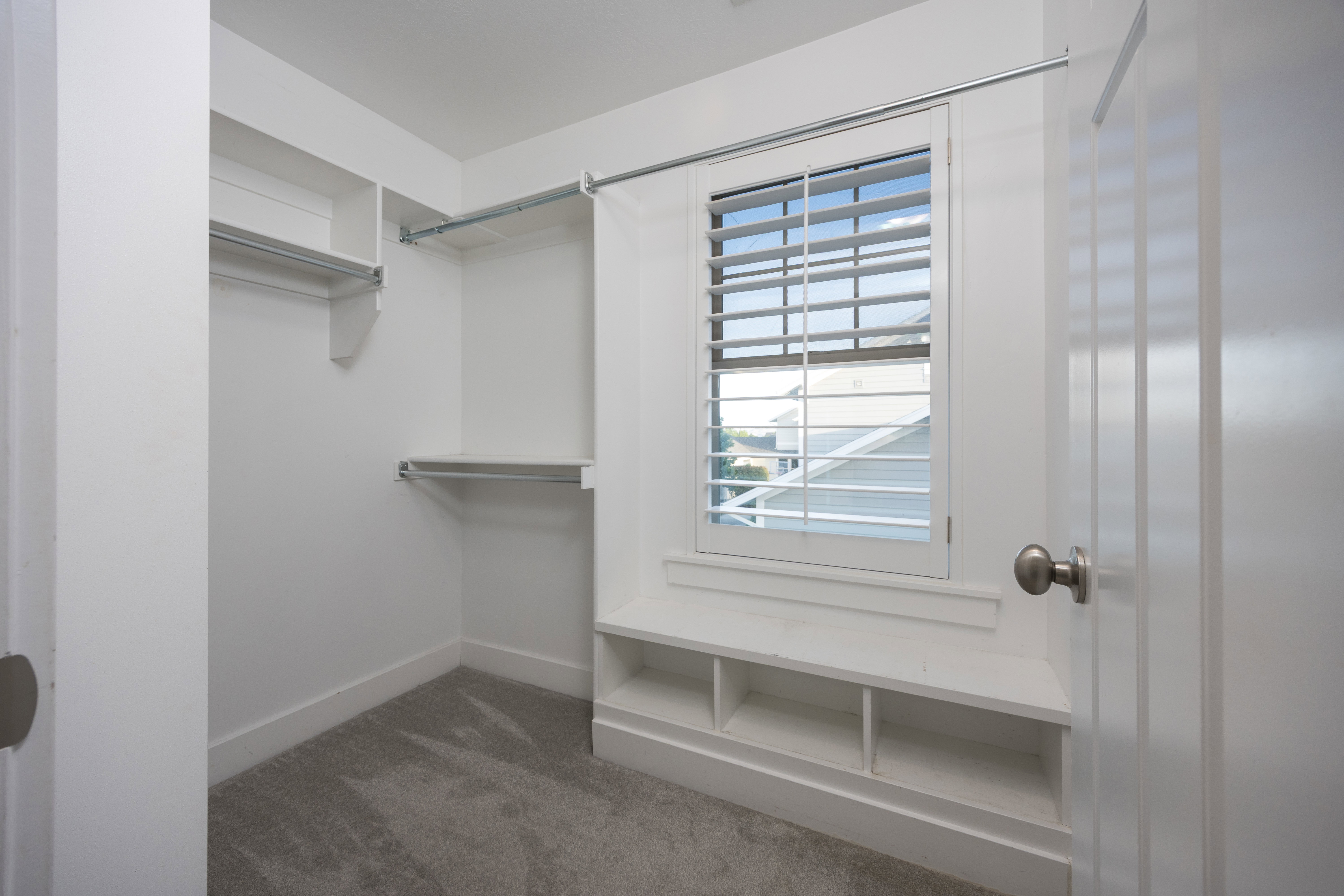 Custom closet system with built-in shelving, hanging rods, and a window featuring plantation shutters