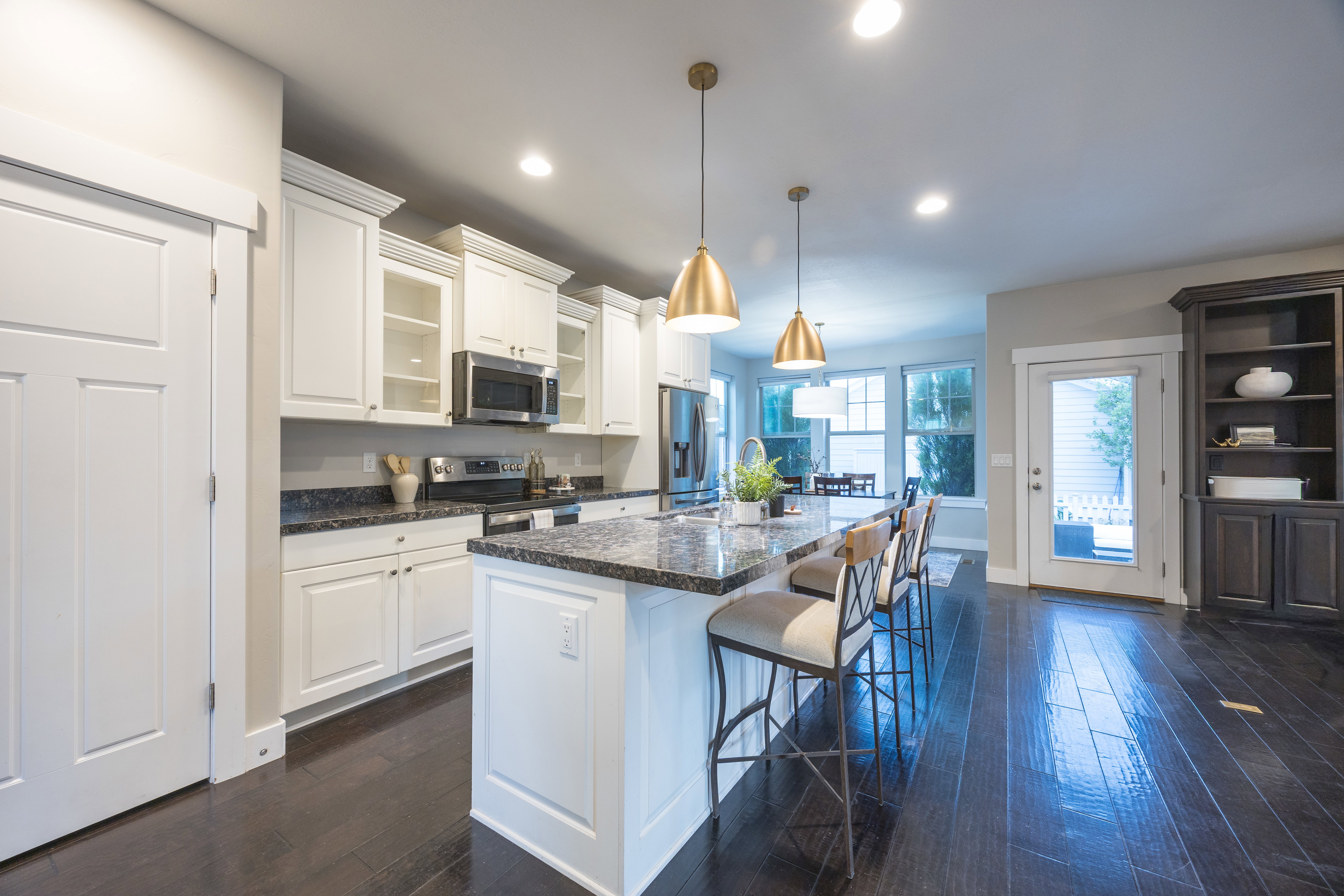 Open-concept kitchen featuring an oversized island with seating, stainless steel appliances, white cabinetry, dark wood-finish flooring, and recessed lighting