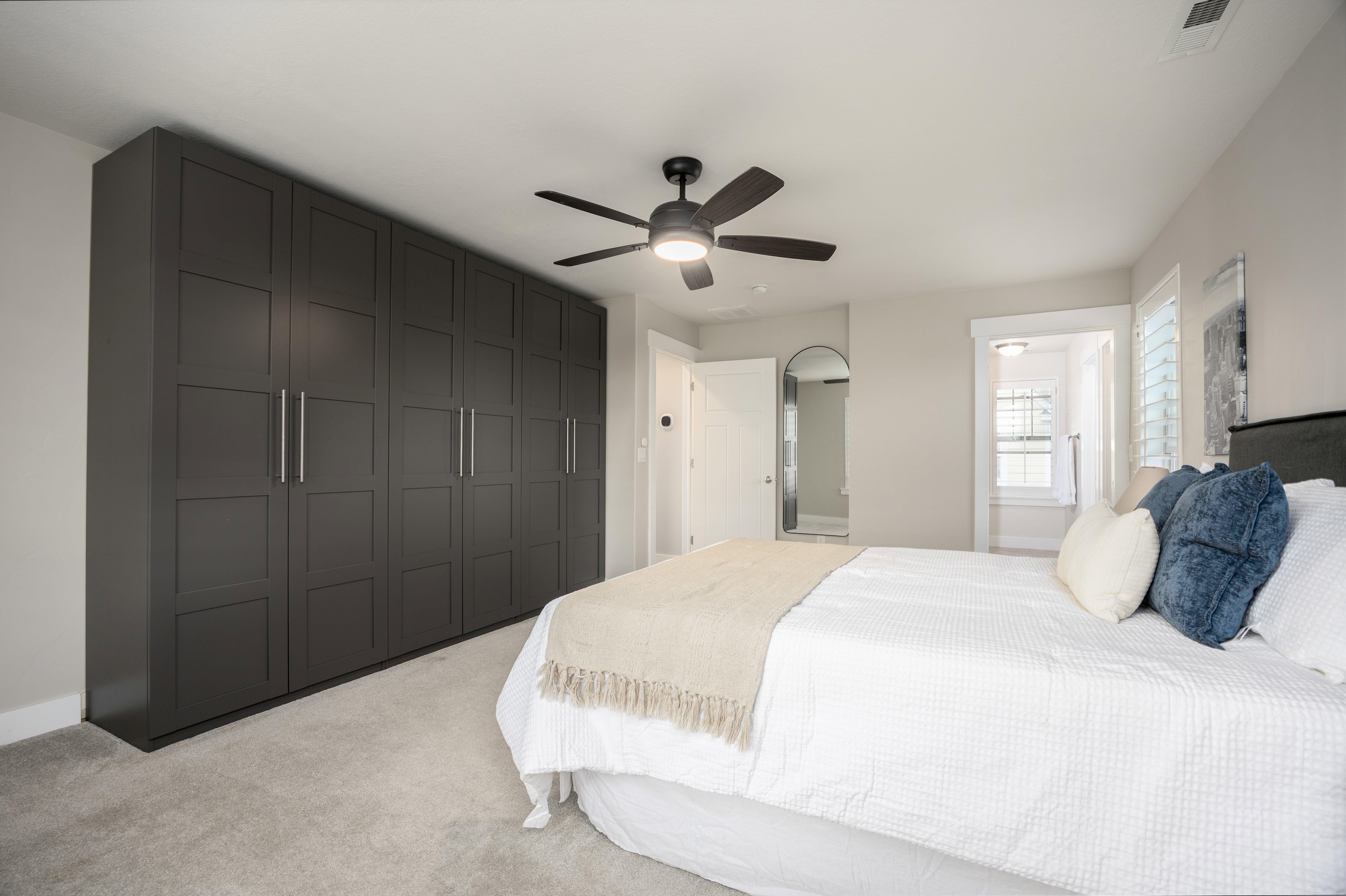 Spacious room featuring extensive built-in cabinetry with panel doors, neutral carpeting, and a ceiling fan with integrated lighting