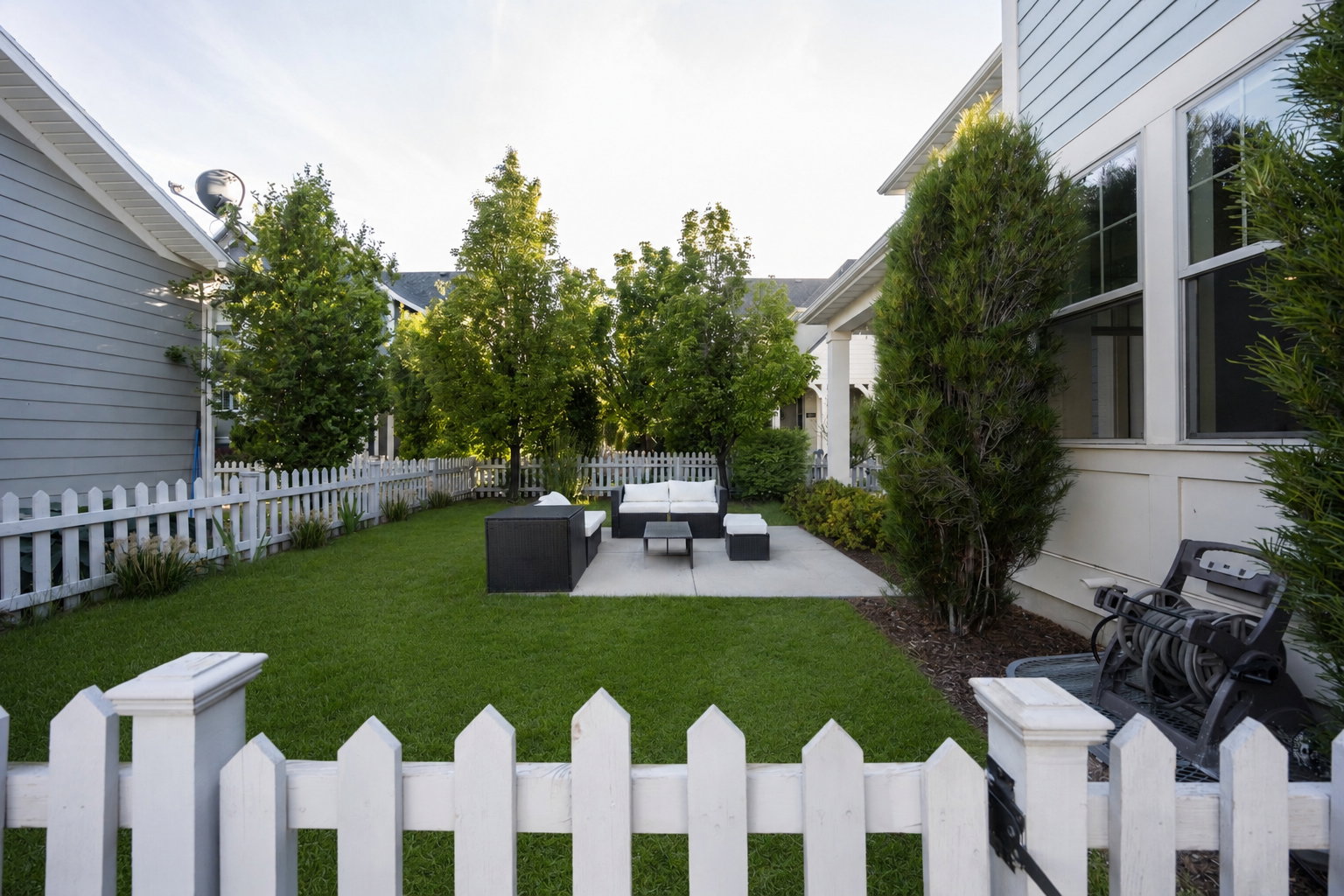 Fenced backyard featuring a concrete patio, expansive lawn, and mature greenery