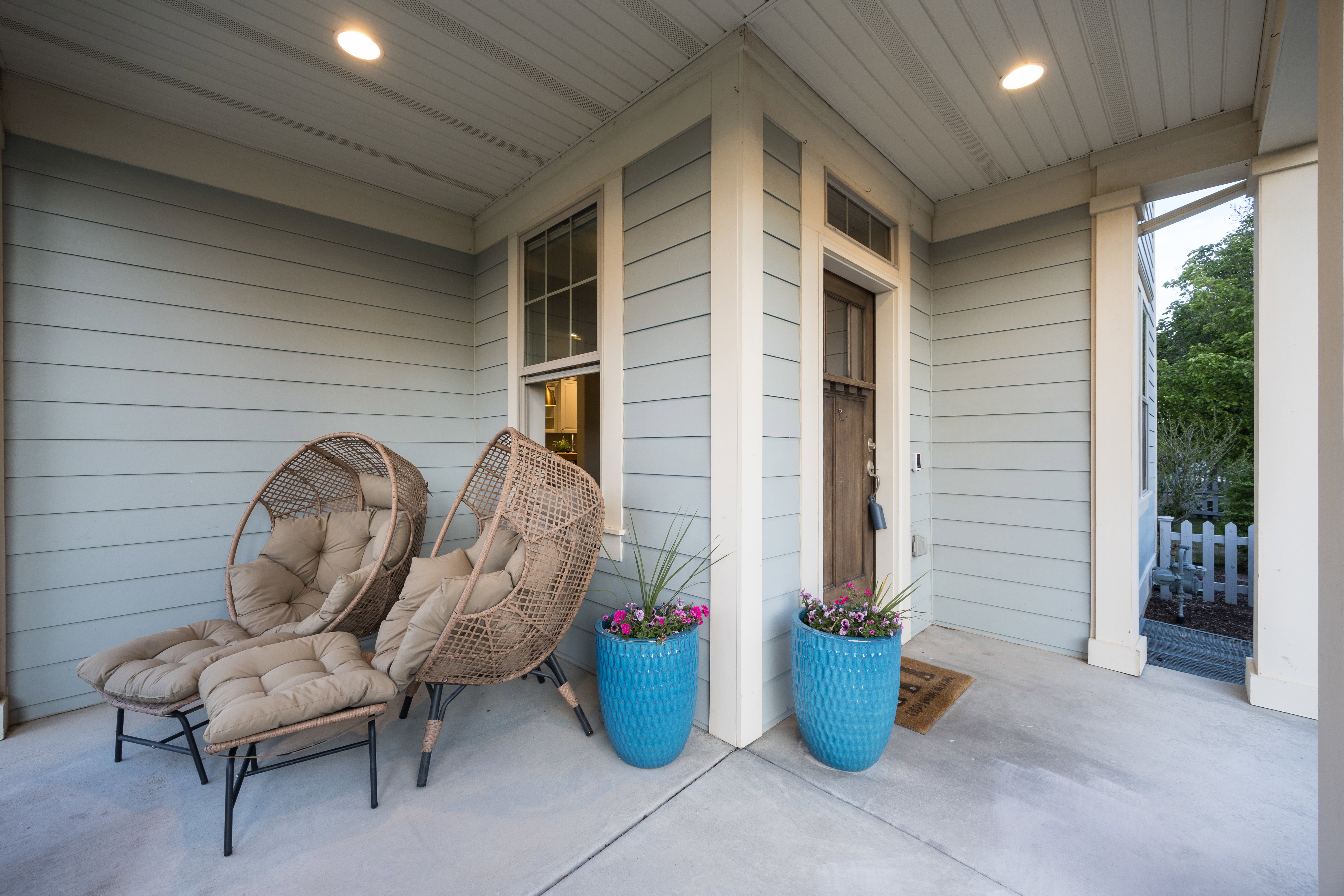 Inviting covered front porch with a wood-finish entry door, light blue siding, and white trim accents