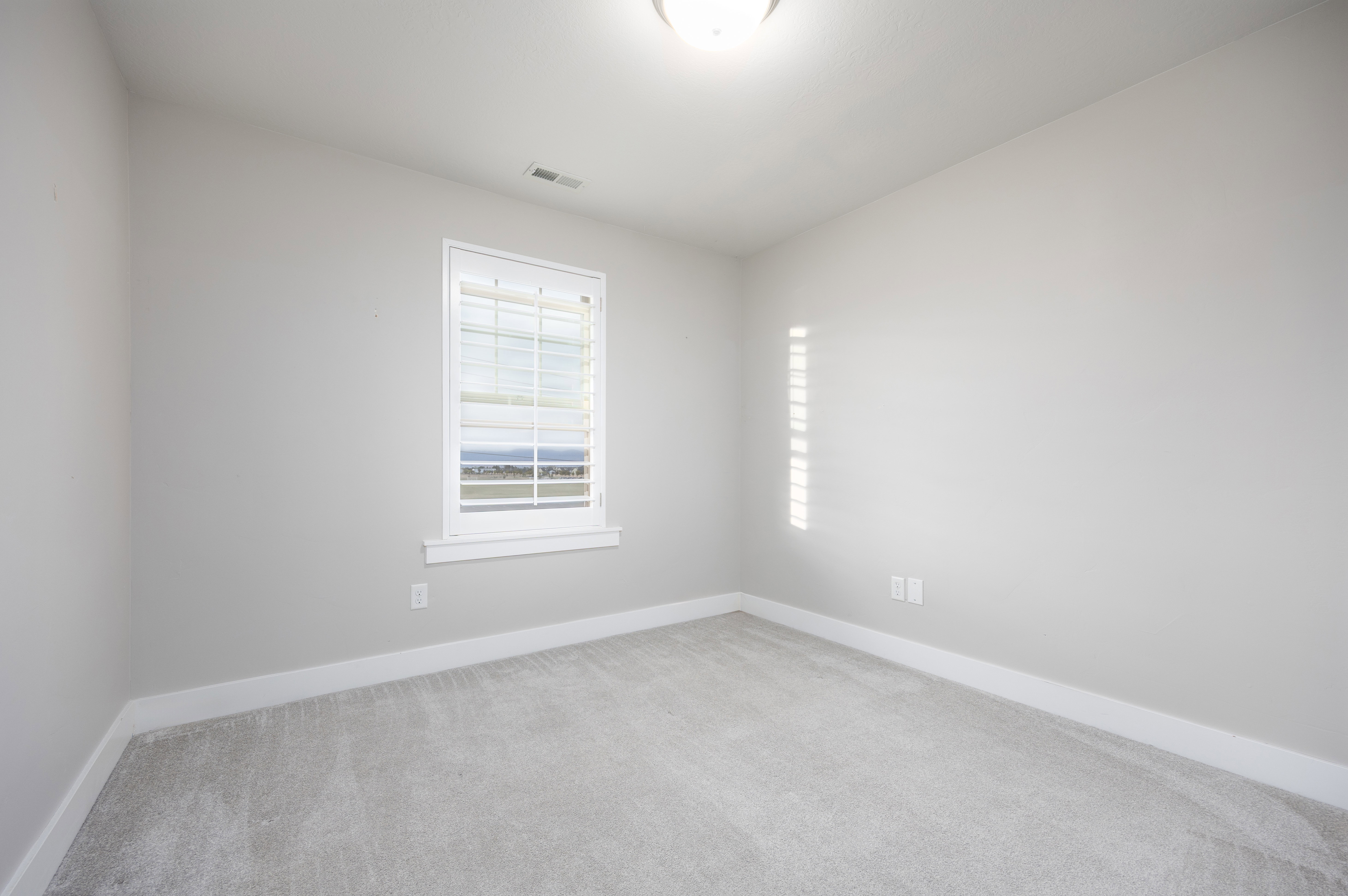 Carpeted room featuring a single window with white plantation shutters, light gray walls, white baseboards, and a flush-mount ceiling light fixture