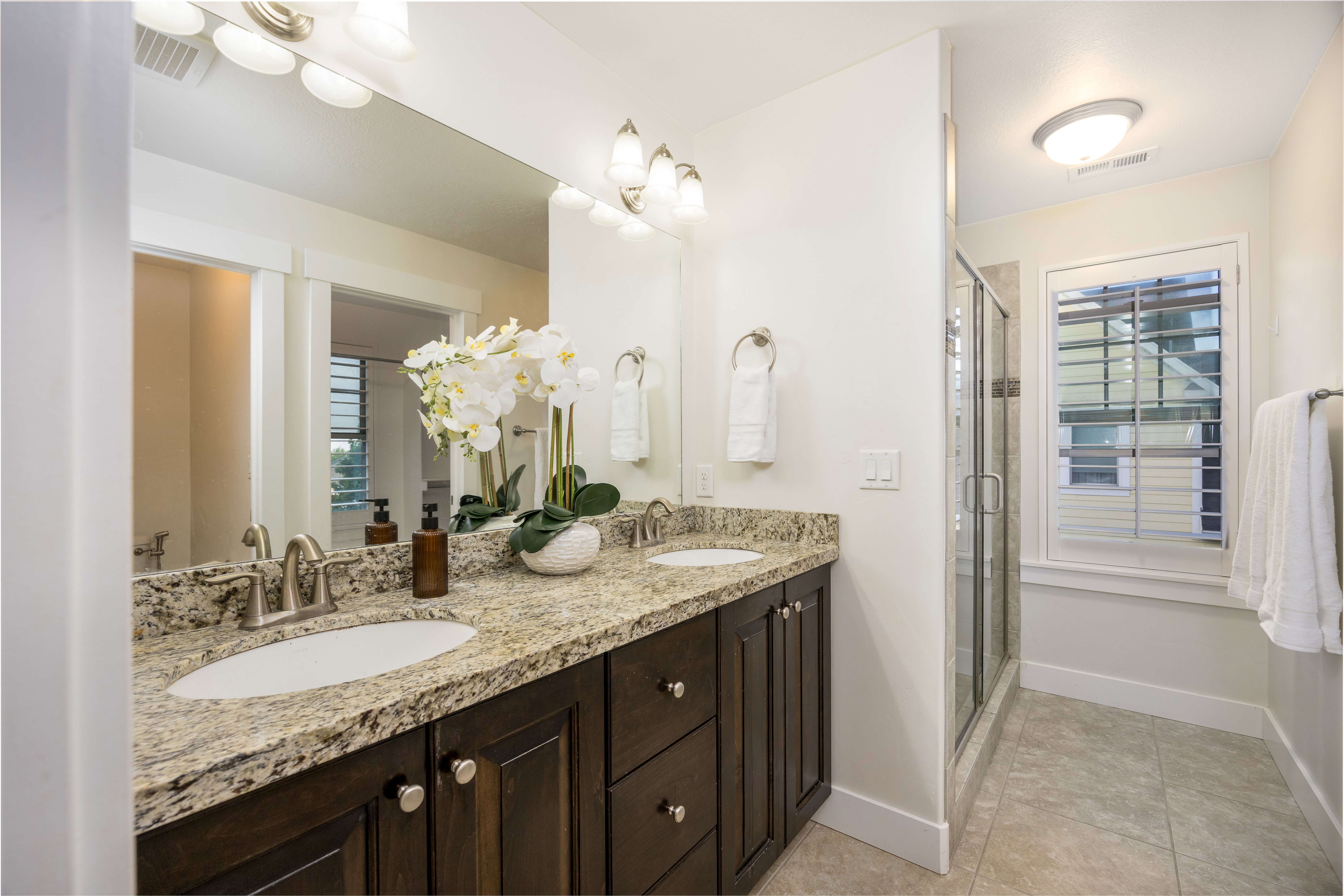 Dual vanity with granite countertops and undermount sinks, espresso cabinetry, brushed nickel hardware, and tile flooring