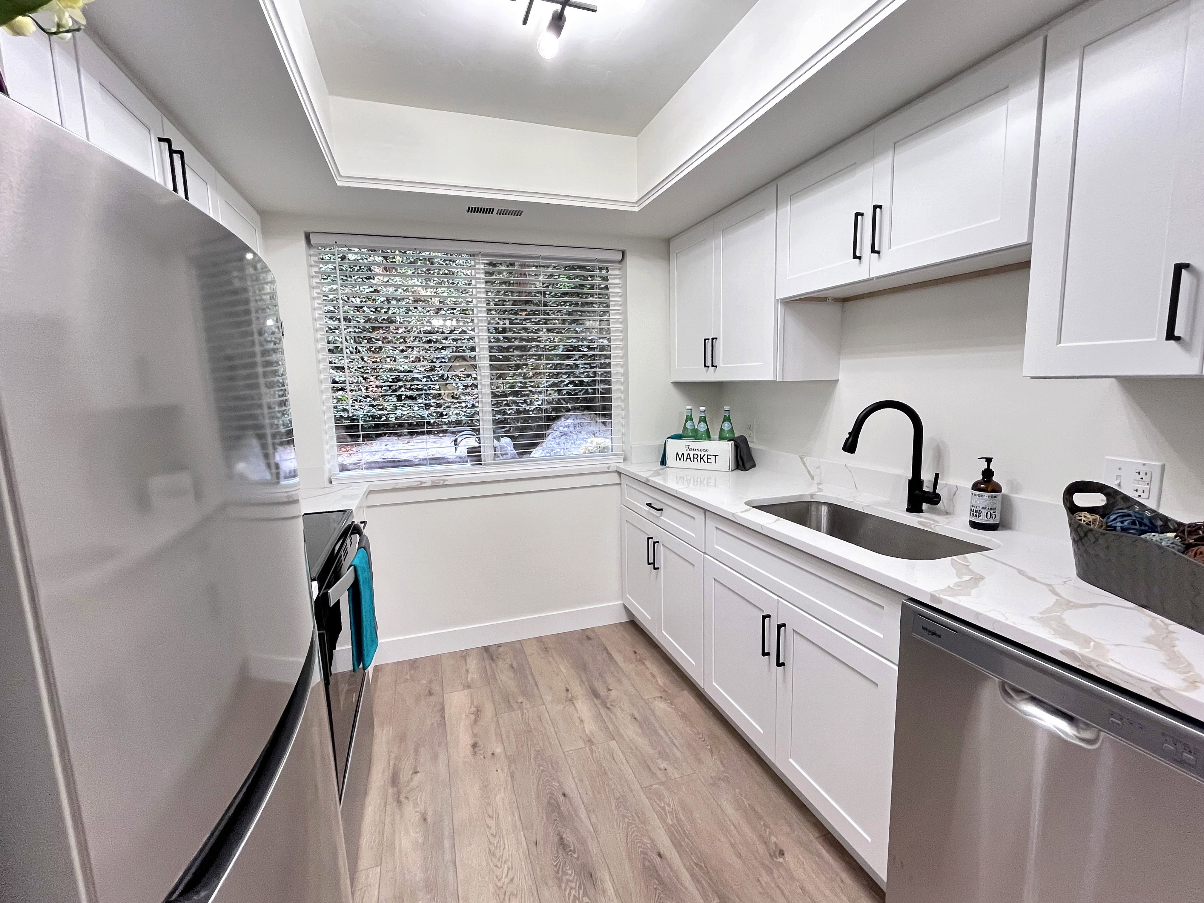 Beautifully renovated kitchen with stainless steel appliances, new white cabinets, light wood finished floors, artistic style ceiling, and light stone counters