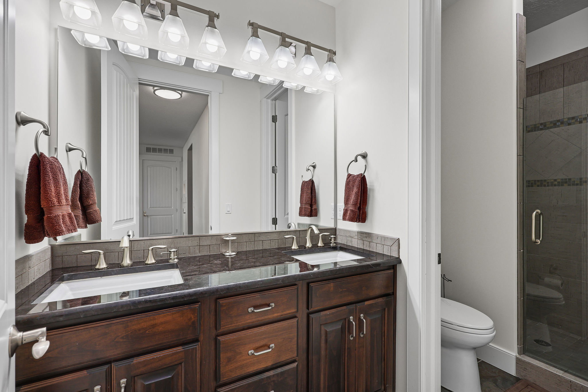 Double vanity featuring dark wood cabinetry, dual undermount sinks, and a dark countertop with a tiled backsplash