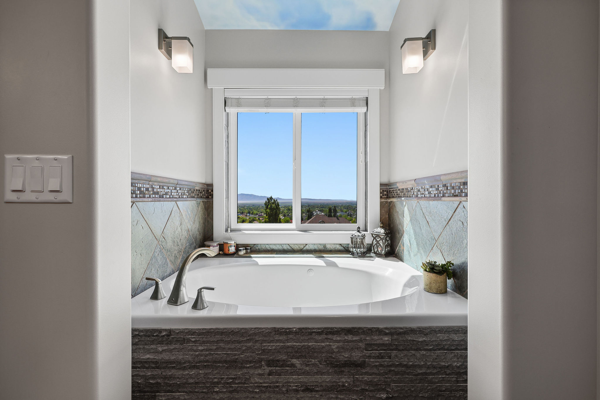 Built-in soaking tub with brushed nickel fixtures, bordered by a tiled surround featuring a mosaic accent strip