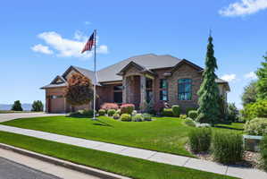 Stone and brick-clad home featuring a multi-gabled roofline, an attached garage with a wood-finish door, a manicured lawn, and mature landscaping