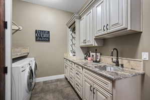 Laundry room featuring extensive custom cabinetry with distressed white finish, a stainless steel sink with a dark bronze faucet, and a stone countertop with a matching backsplash