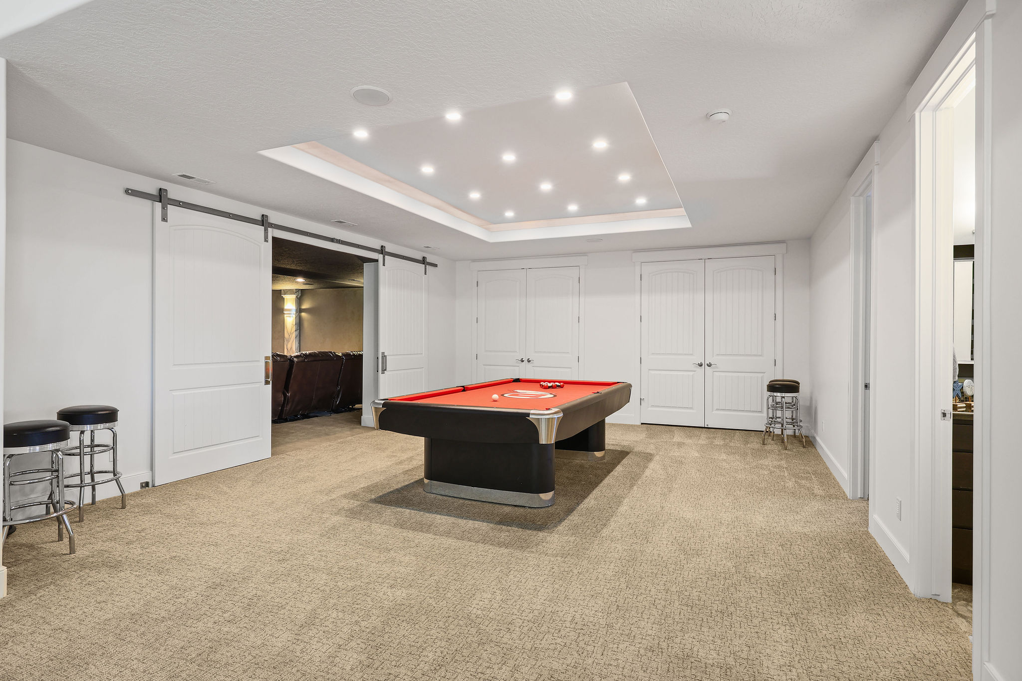 Spacious recreation area featuring plush carpeting, a recessed ceiling with abundant lighting, and a barn door entry