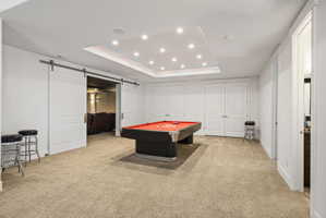 Spacious recreation area featuring plush carpeting, a recessed ceiling with abundant lighting, and a barn door entry