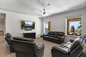 Carpeted entertainment room featuring white walls, a ceiling fan with integrated lighting, and two large windows