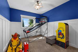 Room featuring board and batten wainscoting with a vibrant blue wall above, a window with white trim, and a ceiling fan with integrated lighting