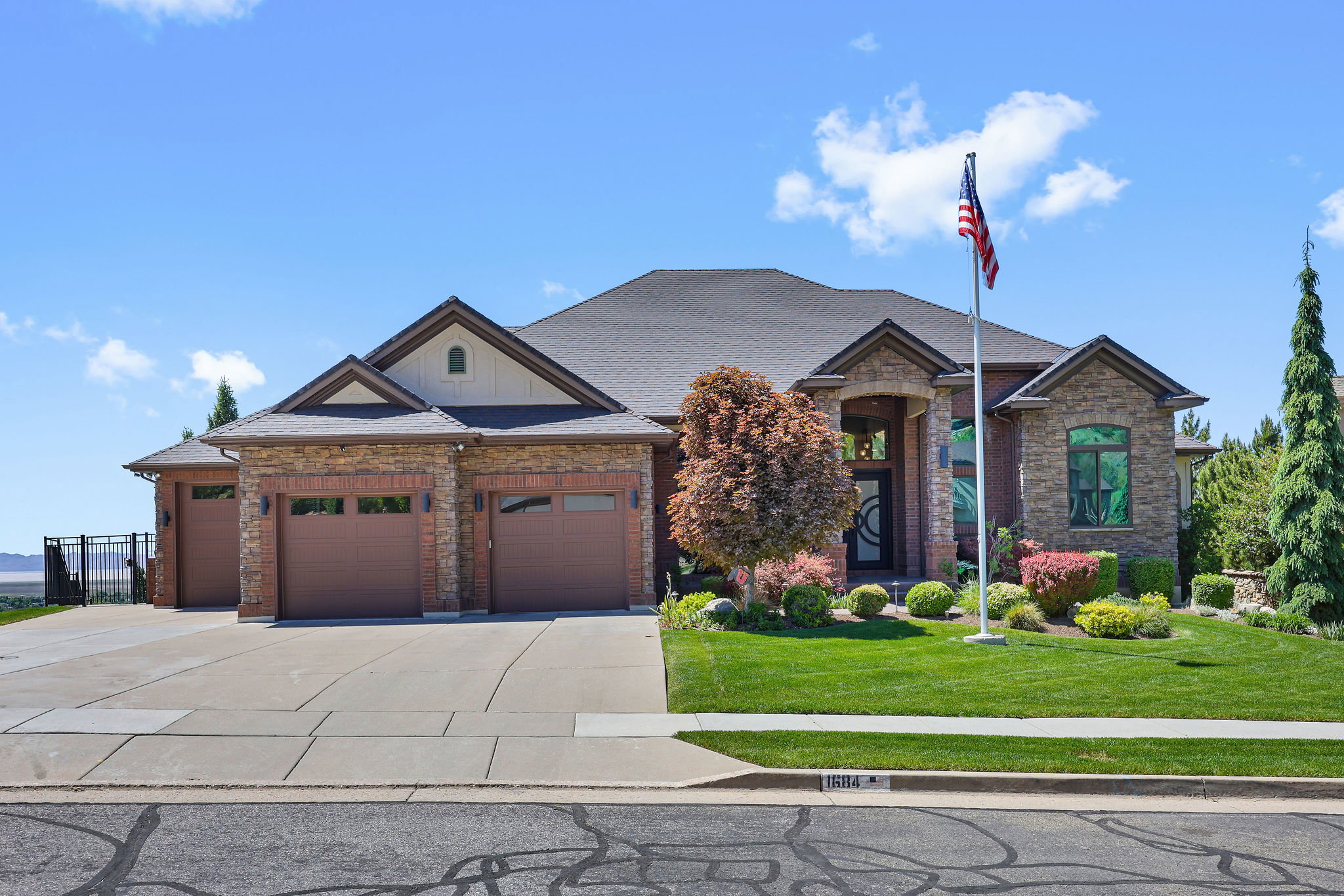 Stone and brick exterior featuring a multi-car garage with individual doors, a concrete driveway, a manicured lawn, and mature landscaping