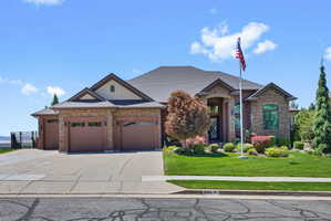 Stone and brick exterior featuring a multi-car garage with individual doors, a concrete driveway, a manicured lawn, and mature landscaping