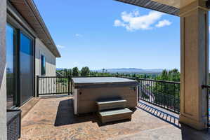 Expansive exterior balcony featuring a hot tub, stamped concrete flooring, and black metal railing