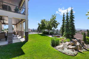 Expansive rear yard featuring a manicured lawn, tiered landscaping with mature evergreens and natural rock, and a fenced perimeter