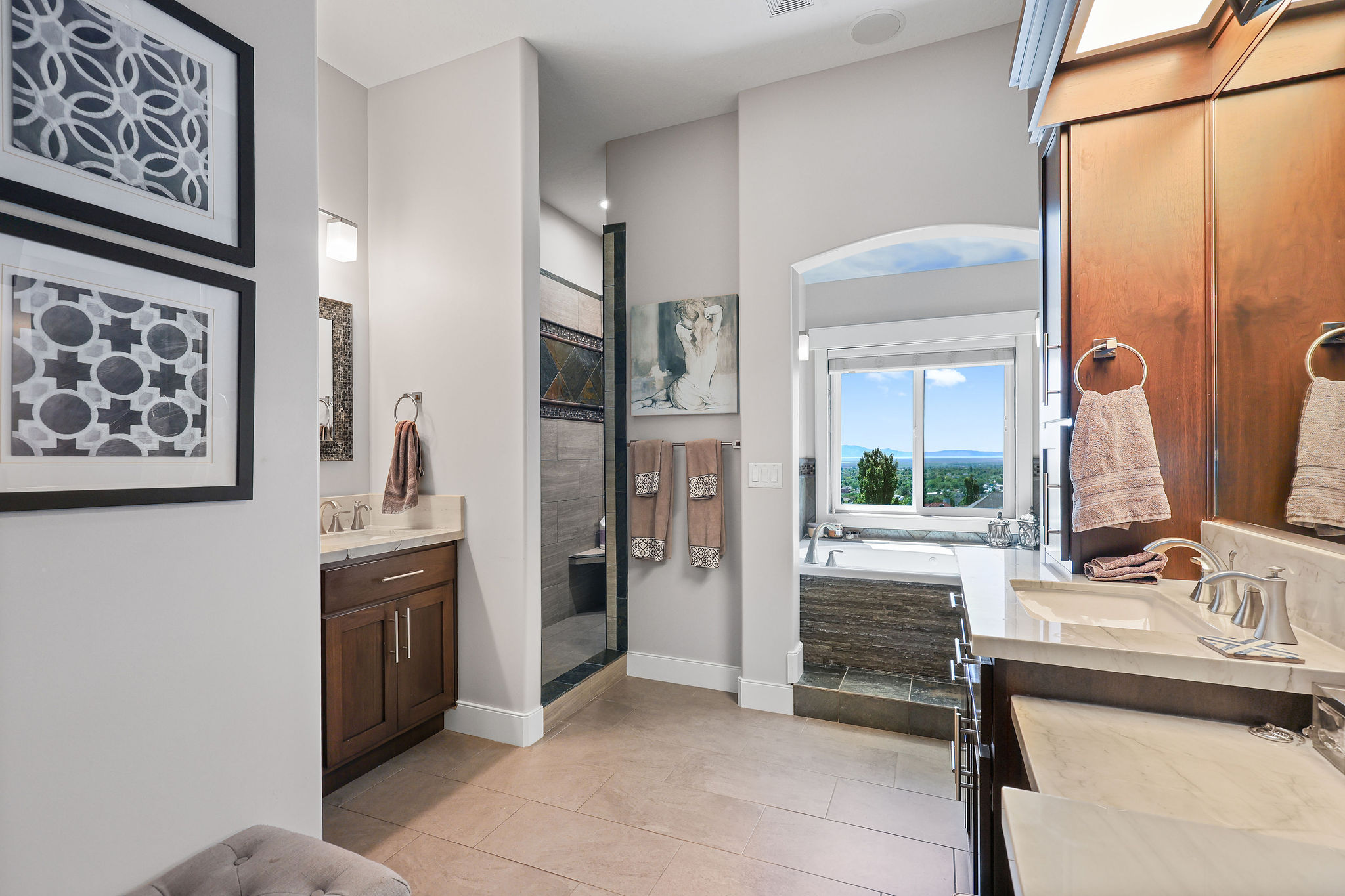 Bathroom featuring dual vanities with integrated sinks, a walk-in shower with decorative tile, a built-in soaking tub, and tile flooring