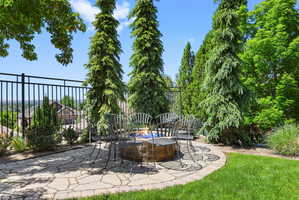 Stone patio featuring a built-in fire pit, surrounded by mature evergreen trees