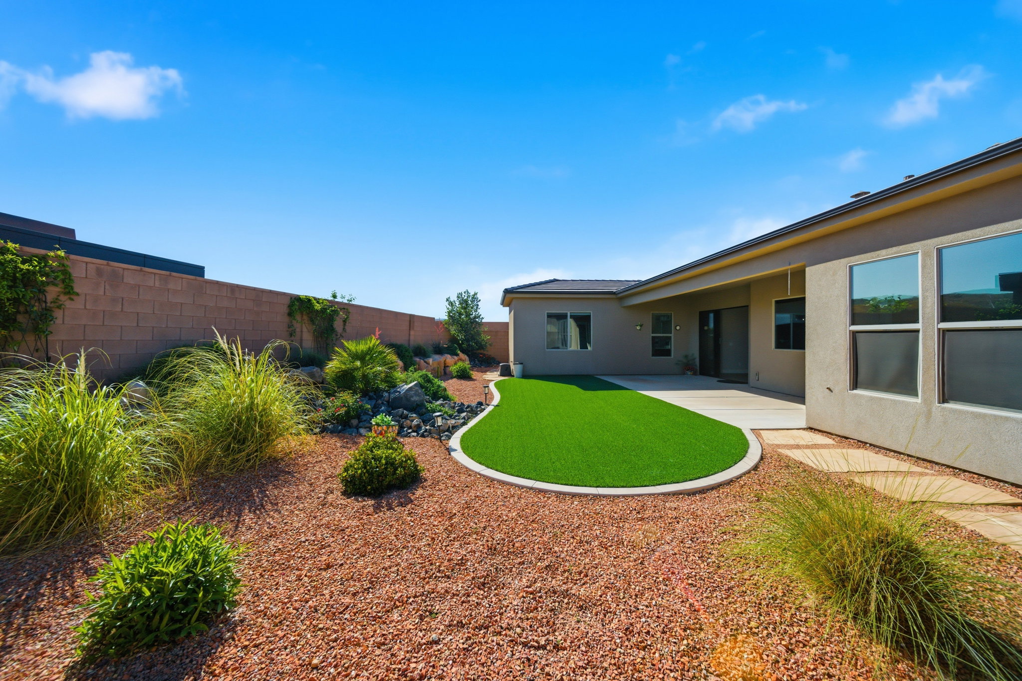 Landscaped backyard featuring an artificial turf lawn, concrete patio, and stone aggregate ground cover