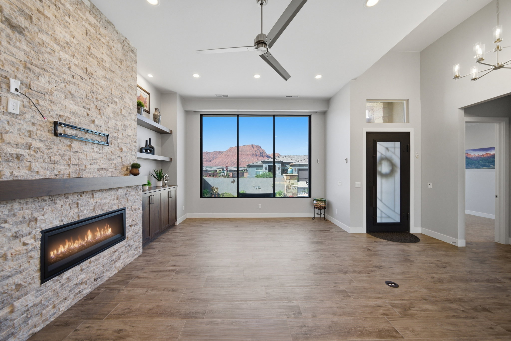 Spacious living area featuring a stacked stone fireplace, a contemporary ceiling fan, and large windows