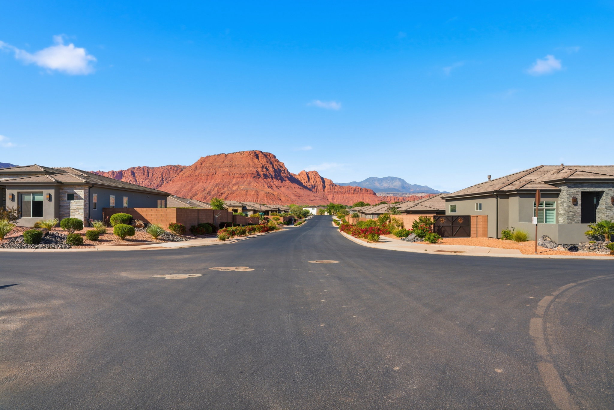 Paved neighborhood street with single-story homes featuring stucco and stone exteriors, and tile roofs