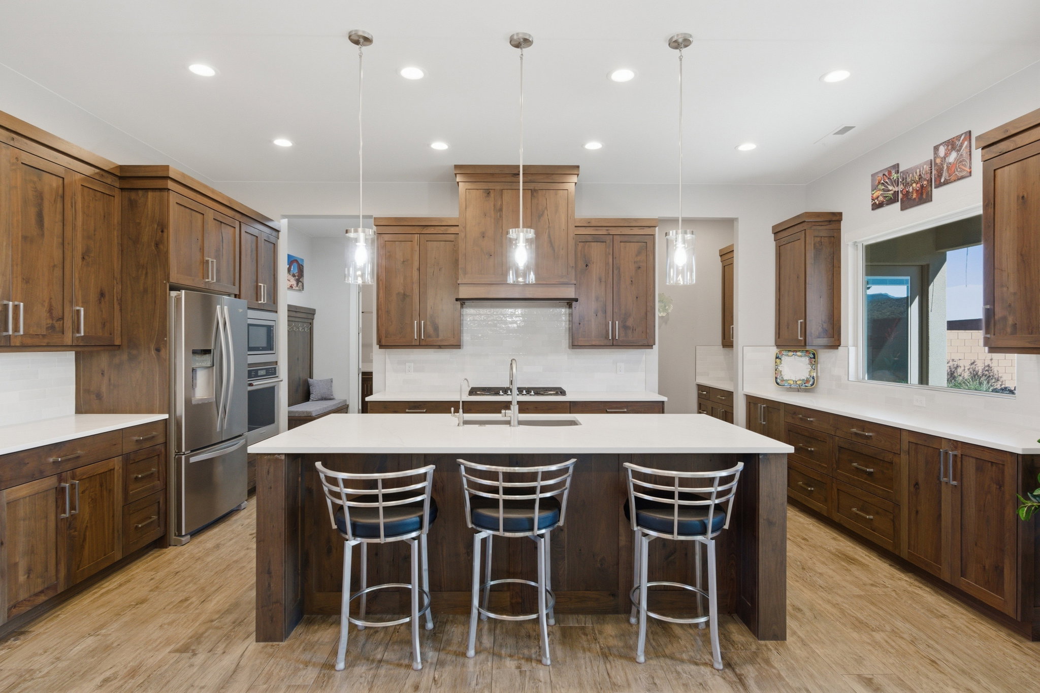 Spacious kitchen featuring an expansive center island with a light-toned countertop, rich wood-finish cabinetry, stainless steel appliances, a white subway tile backsplash, and wood-finish flooring