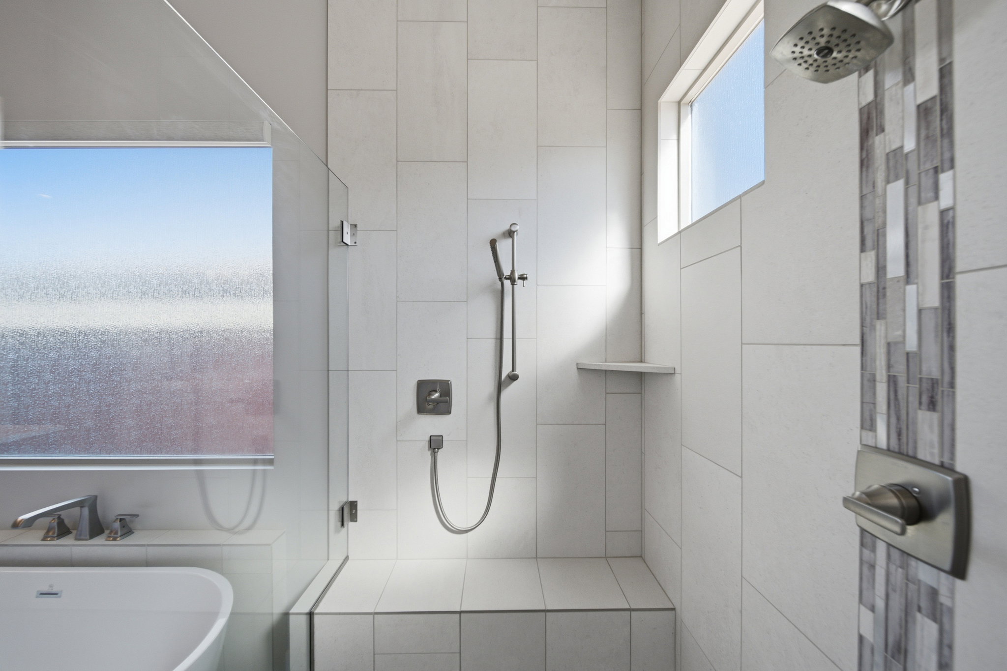 Walk-in shower featuring light-toned tile walls, a built-in bench, and a niche shelf